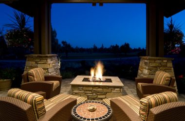 Image of an evening scene showing a glowing gas fire pit under covered patio with comfortable outdoor chairs arranged around the flames for cozy nighttime gathering.