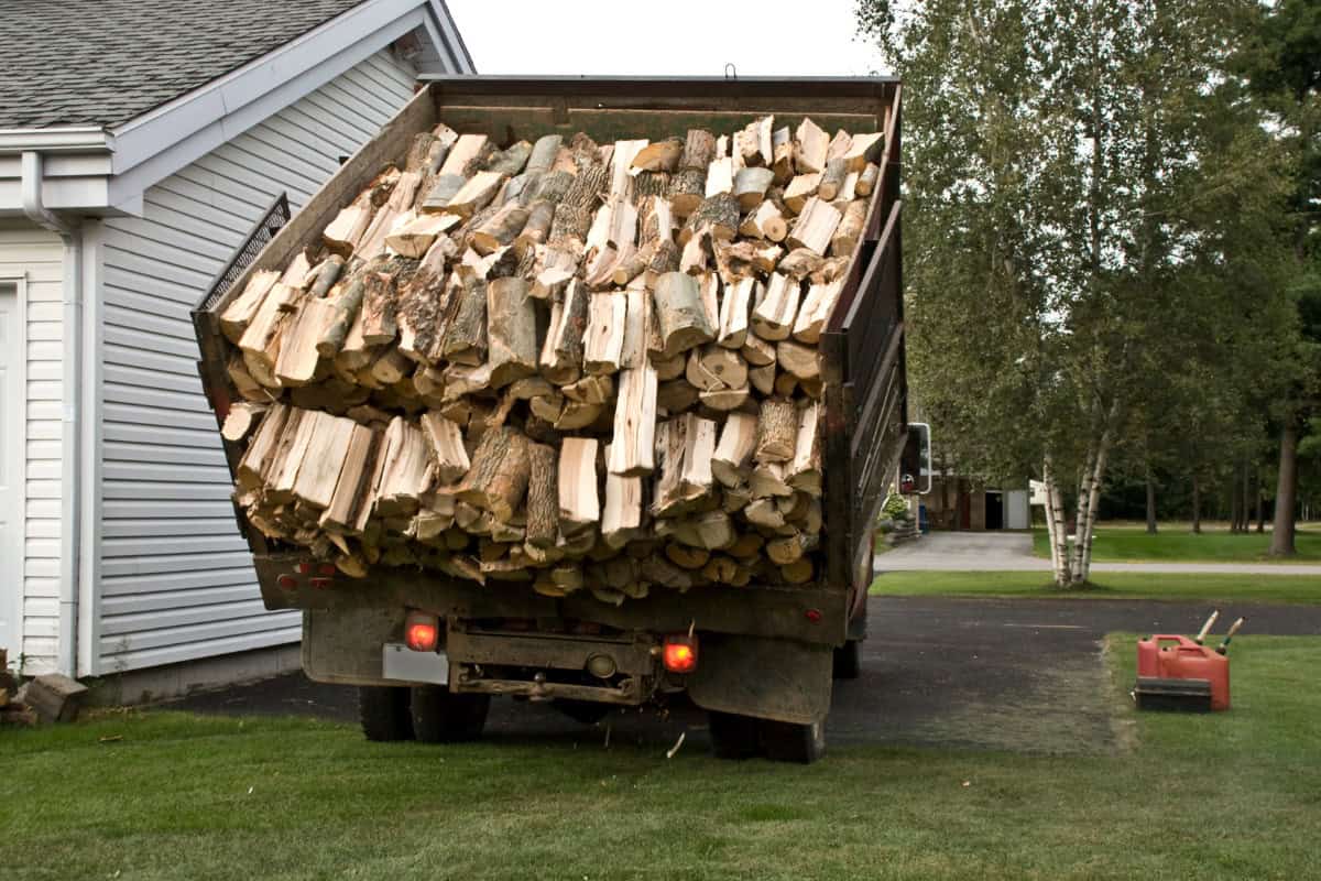 us-firewood-prices-main Image of a firewood delivery truck dumping wood on a home's lawn for a blog post on U.S. firewood prices.