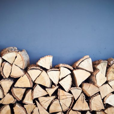 Image of a stack of firewood against a blue background for a blog post answering the question "what is a rick of firewood."