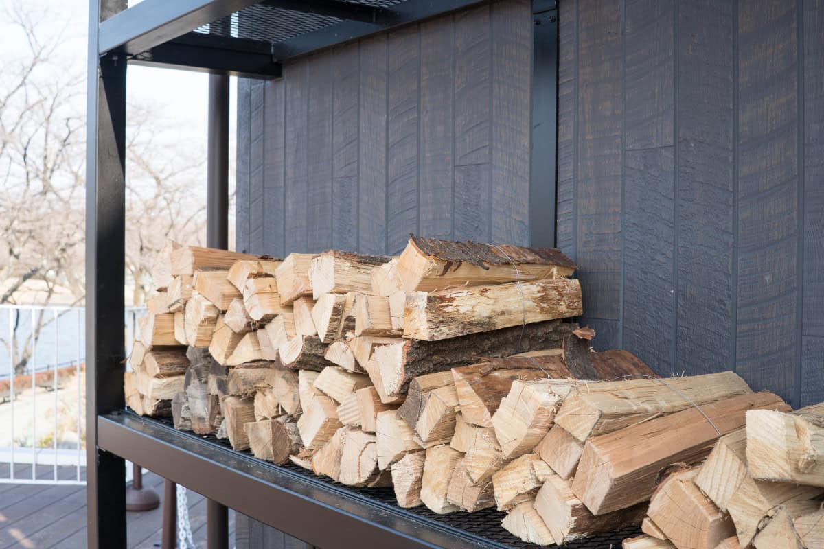 Safety Tips for Using Fire Pits Image of firewood on an outdoor storage rack for a blog post about kiln dried firewood for fire pits