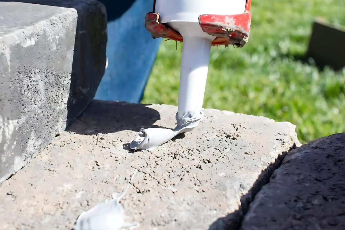 fire-pit-adhesives-understanding Image of a man applying construction adhesive to a fire pit paver.