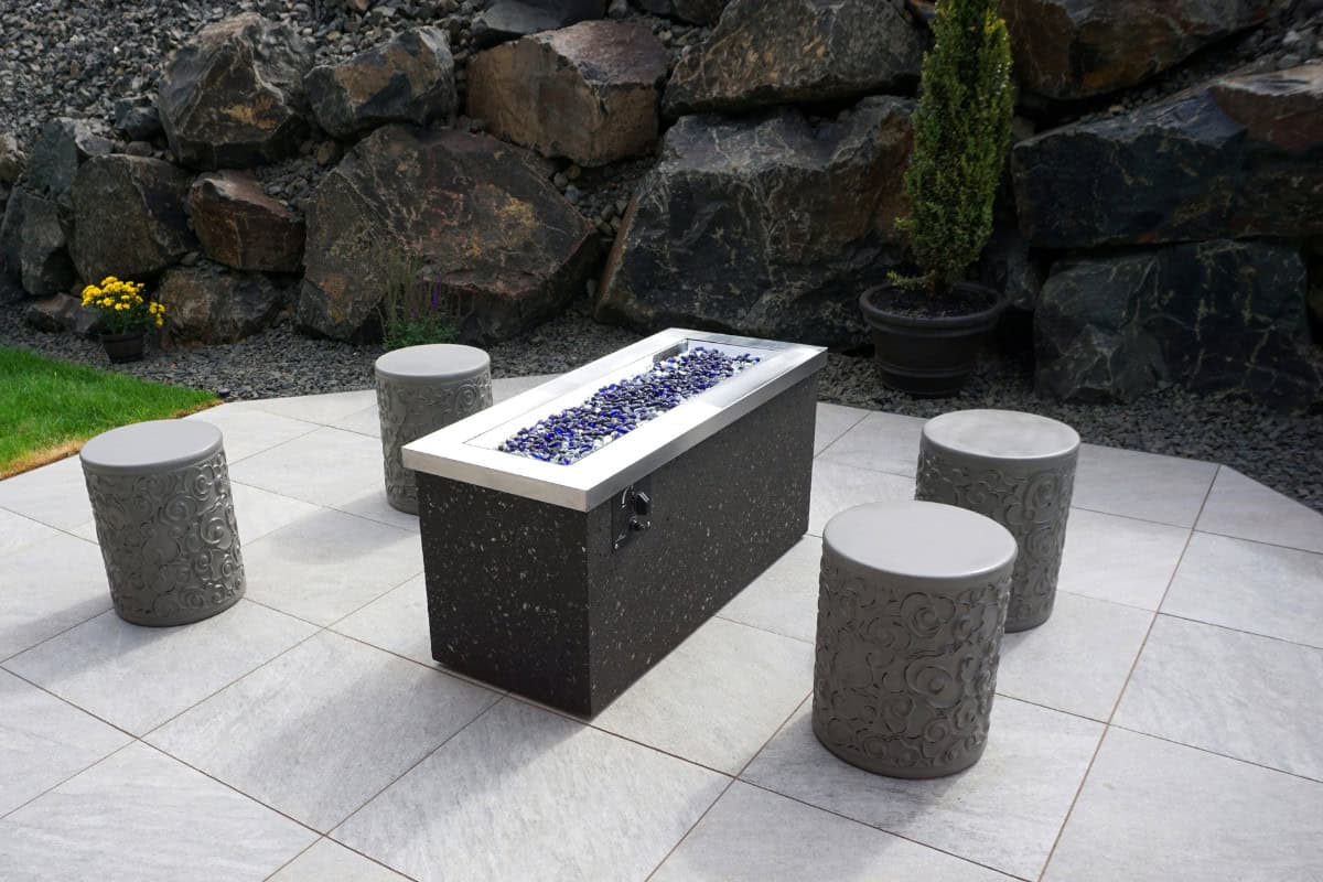 Using a Fire Glass Calculator Image of a gas fire pit with stone stools for a blog post discussing how much fire glass is needed for a fire pit.