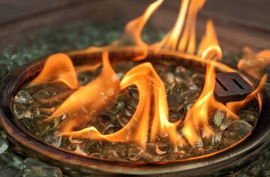 Image of a fire pit's burner ring surrounded by clear fire glass for a blog post discussing how much fire glass is needed for fire pits.