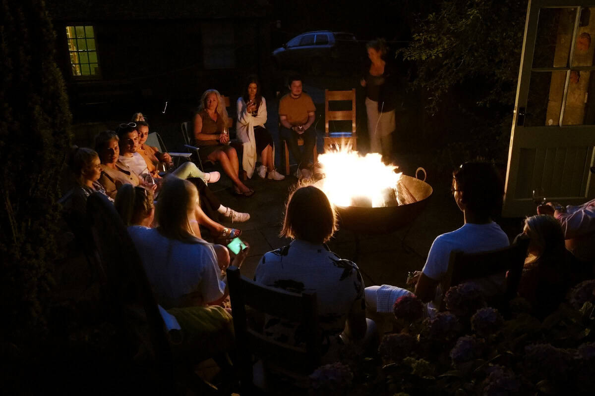 Why Size Matters for Fire Pit Accessories Image a large group of people around a fire pit at night.