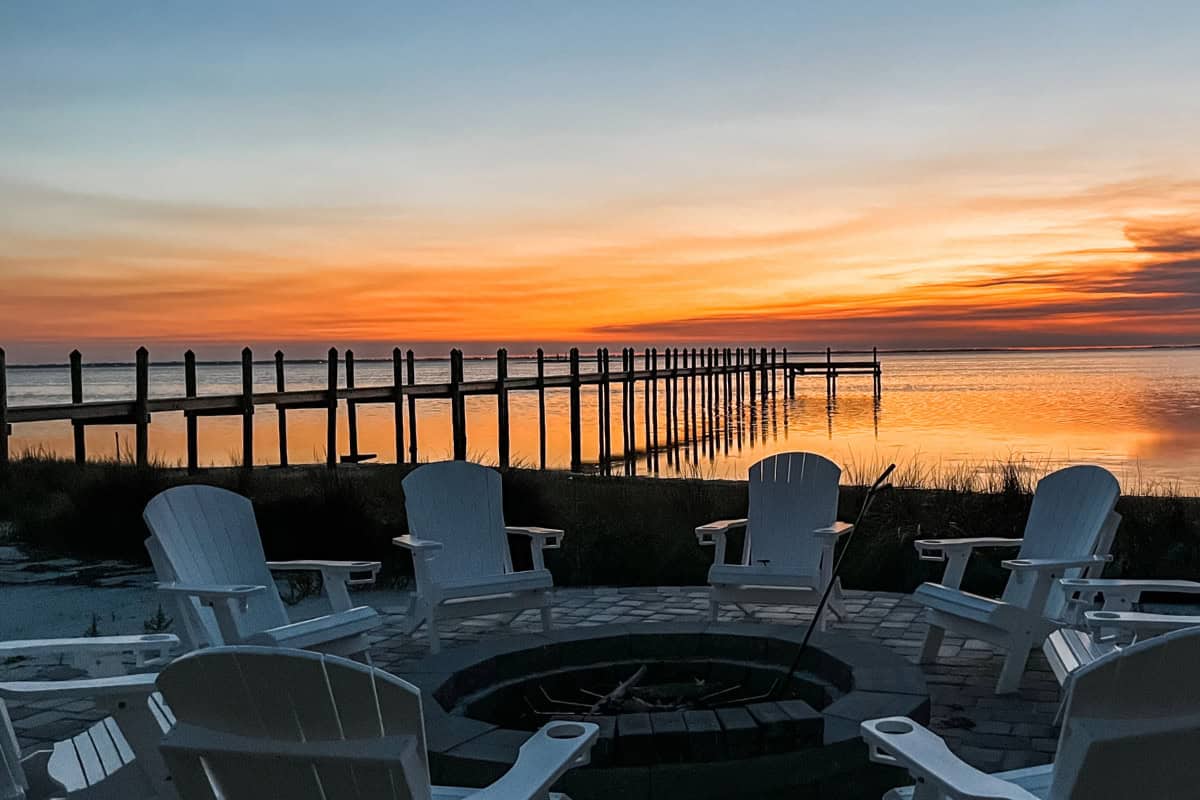 fire-pit-seating-ideas-faqs Image of a fire pit and chairs by a river at sunset.