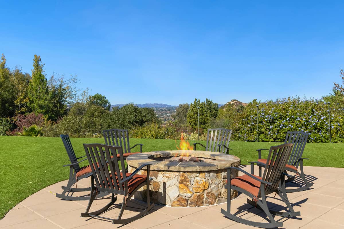 gas-fire-pits-provide-heat-do Image of rocking chairs around a gas fire pit during a sunny day.