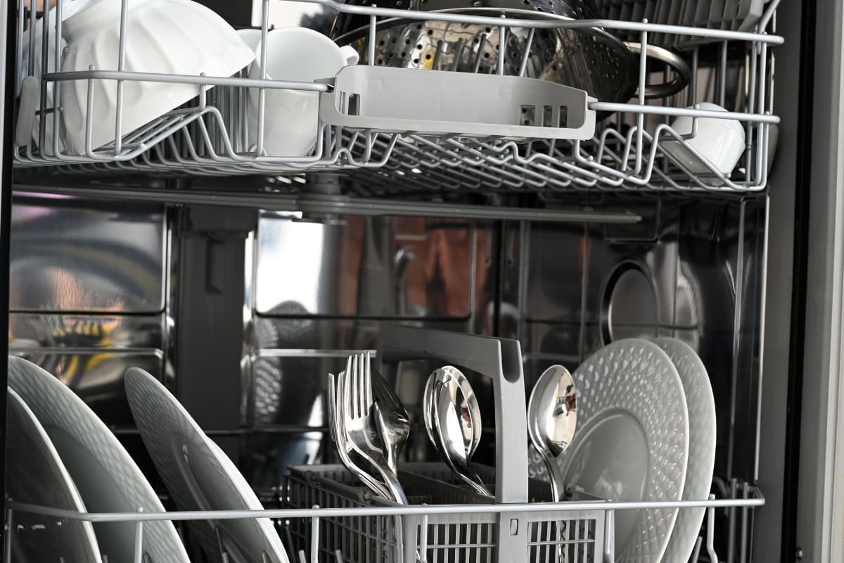 how-to-clean-fire-glass-faqs Shiny dishwasher filled with clean white dinnerware, utensils, and glasses ready for the next meal, showcasing organized dishware storage and modern kitchen design.