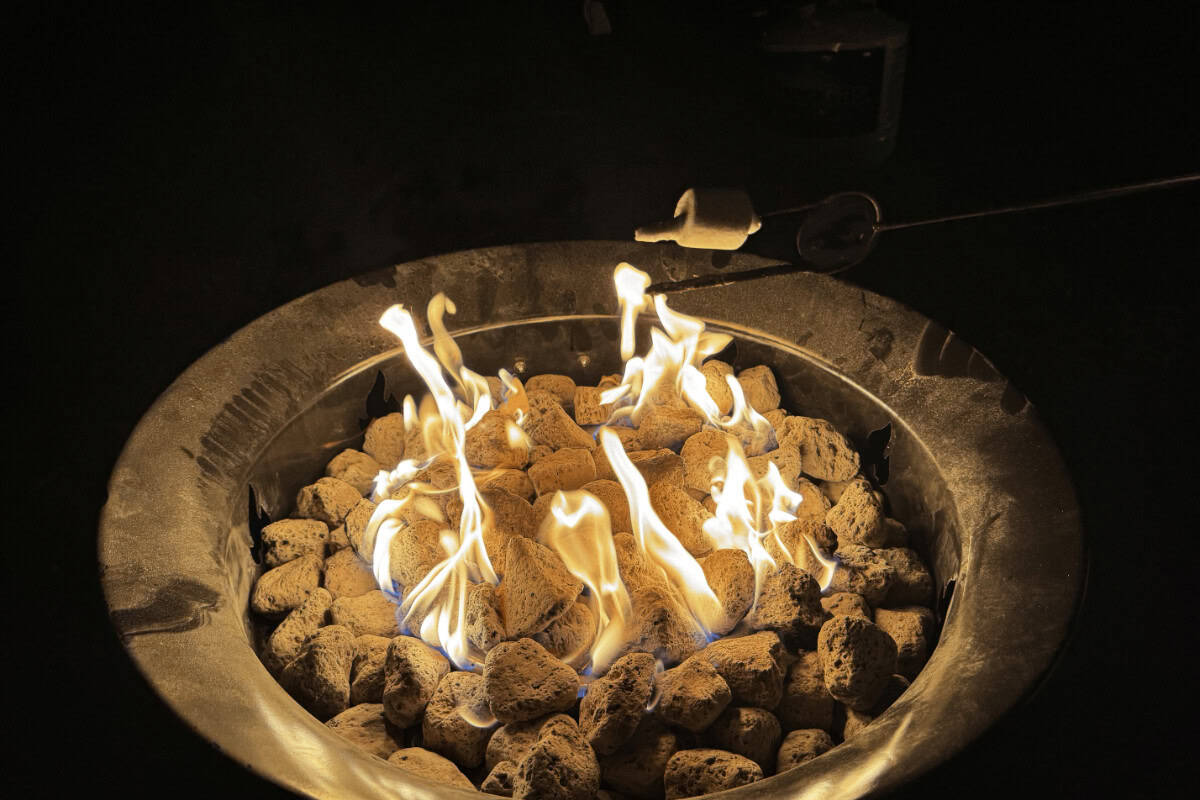 outland-living-mega-fire-pit-review-heat-output Image of a gas fire pit at night with a marshmallow roasting for a Outland Living Mega review.