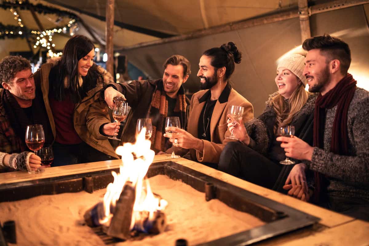 fire-pit-under-covered-patio-choosing Cozy outdoor fire pit gathering with friends, warm drinks, and holiday decor, perfect for backyard entertaining in fall or winter.