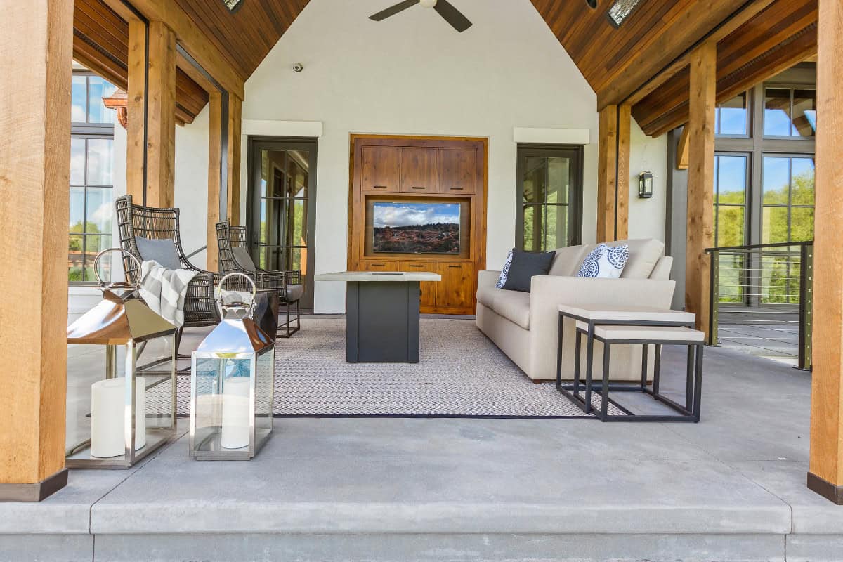fire-pit-under-covered-patio-closing Modern outdoor lounge with cozy seating, TV, and fireplace in backyard patio area.