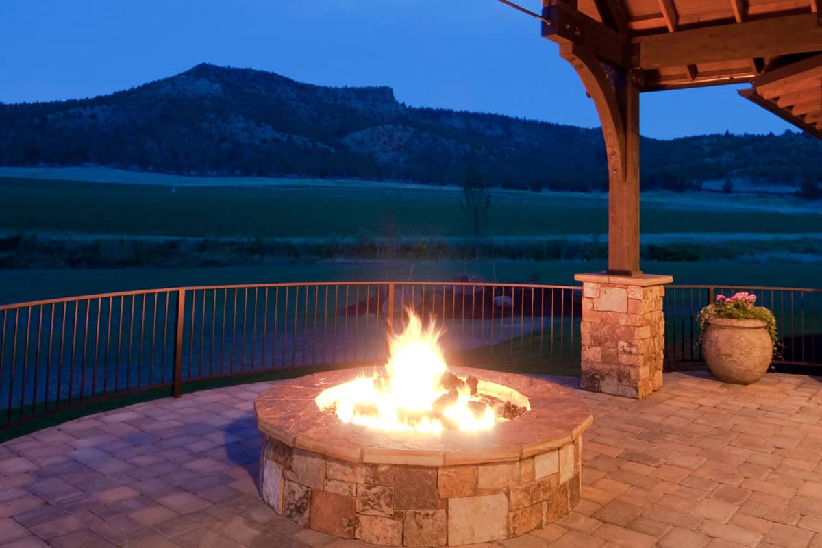 fire-pit-under-covered-patio-main Cozy outdoor fireplace on a scenic mountain landscape porch with stone accents and a potted plant, perfect for backyard gatherings and outdoor entertainment.