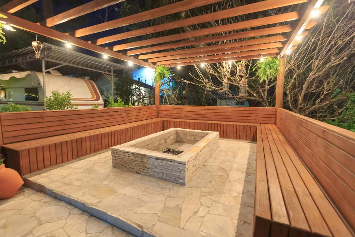 fire-pit-under-covered-patio-ventilation Cozy outdoor backyard fire pit area with wooden seating and string lights at night, perfect for outdoor gatherings and relaxing evenings.