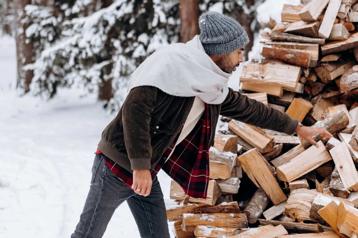 Image of a man gathering firewood from large pike during a snowy winter day.