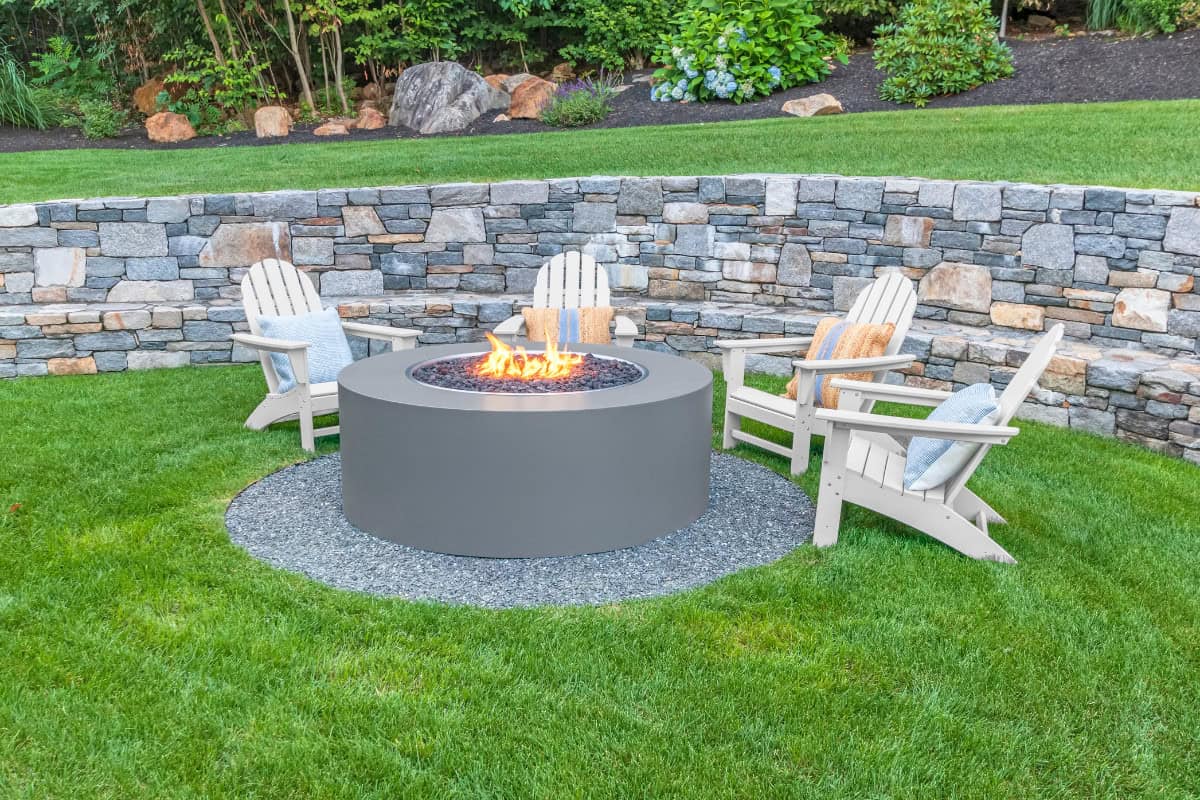 gas fire pit problems-installation Fire pit outdoor backyard with seating area - Backyard Toasty fire pit setup featuring Adirondack chairs in a landscaped garden with a stone retaining wall and lush green grass.