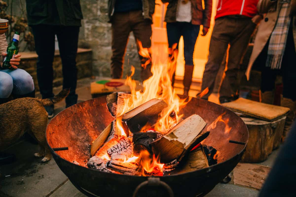 uk-firewood-prices-planning Image of a group of people standing around a burning fire pit on a cool day.