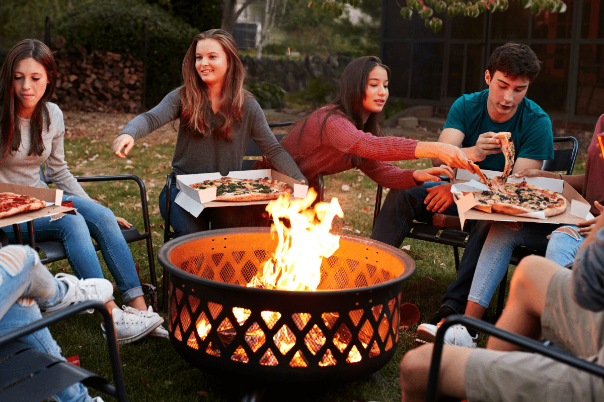 fire-pit-safety-statistics-main-min Image of a group of teenagers eating pizza around the fire pit for an article covering fire pit safety statistics.